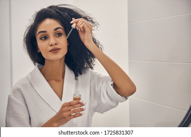 Portrait Of A Gorgeous Woman Applying A Facial Serum To Her Skin Before The Mirror