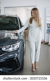 Portrait Of Gorgeous Woman In Showroom. Beautiful Salesperson Standing By Car. Blond Hair Female After Buying Car