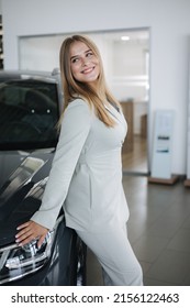 Portrait Of Gorgeous Woman In Showroom. Beautiful Salesperson Standing By Car. Blond Hair Female After Seles Car