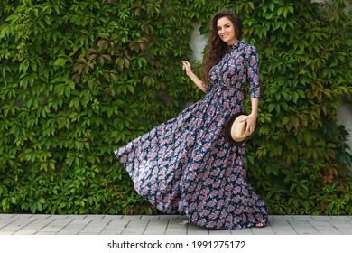 Portrait of gorgeous woman wearing beautiful maxi dress posing against wall with a wild grape