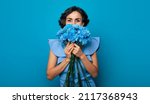 Portrait of a gorgeous woman, who is looking in the camera and hiding a part of her face over the bunch of blue flowers. Mothers day. Women