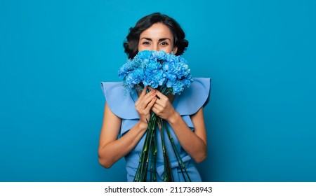Portrait of a gorgeous woman, who is looking in the camera and hiding a part of her face over the bunch of blue flowers. Mothers day. Women's holidays. Springtime. Women rights. The 8th of March