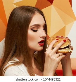 Portrait of gorgeous young woman with closed eyes and red lips holding tasty cheeseburger and biting it. Attractive female model eating burger with pleasure. Beautiful girl enjoying fast food meal. - Shutterstock ID 1044493321