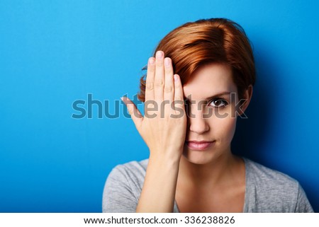 Portrait of a Gorgeous Young Woman Covering Half Face with Hand and Looking at the Camera Fiercely Against Blue Wall with Copy Space.