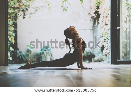 Portrait of gorgeous young woman practicing yoga indoor. Beautiful girl practice cobra asana in class.Calmness and relax, female happiness.Horizontal, blurred background