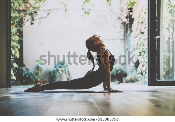 Portrait of\
gorgeous young woman practicing yoga indoor. Beautiful girl\
practice cobra asana in class.Calmness and relax, female\
happiness.Horizontal, blurred\
background