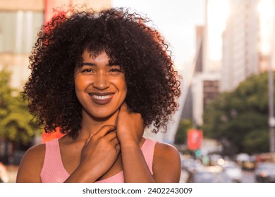 Portrait of gorgeous young woman in the shade of tree with big smile and hands around neck. Urban background in Sao Paulo City during summertime. - Powered by Shutterstock