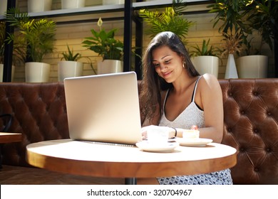 Portrait of gorgeous young woman sitting with open laptop computer in modern coffee shop, female freelancer using net-book for distance work, student girl learning on portable gadget device