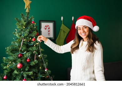 Portrait Of A Gorgeous Young Woman Smiling While Putting Up The Christmas Lights On The Tree 