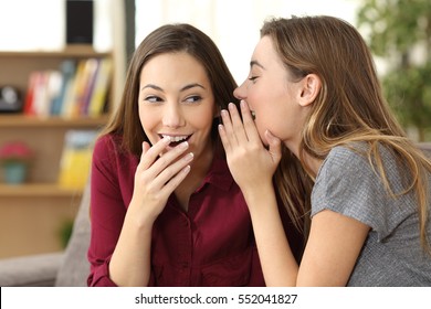 Portrait of a gossip girl telling a secret in the ear to her friend sitting on a couch at home