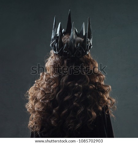 Portrait of a Gothic Princess. Beautiful young brunette woman in metal crown and black cloak. back view