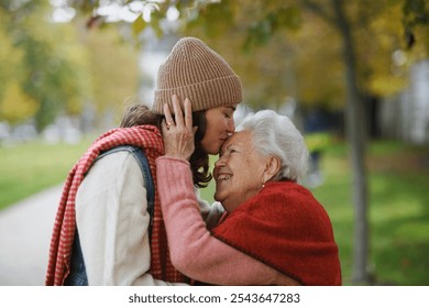 Portrait of a granddaughter on autumn walk in the park with her grandmother, kissing her forehead. - Powered by Shutterstock