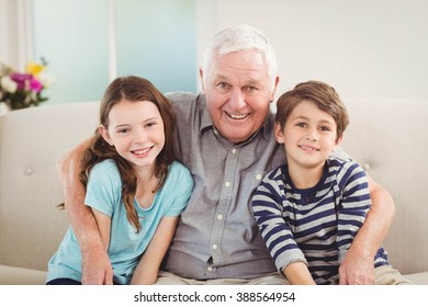 Portrait of grandfather and grandchildren sitting together on sofa in living room - Powered by Shutterstock