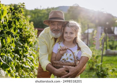 Portrait of grandfather with granddaughter granddaughter picking rasberries from the bush, spending time outdoor in garden. - Powered by Shutterstock