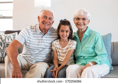 Portrait Of Grandmother And Grand Father With Their Granddaughter Sitting On Sofa In Living Room