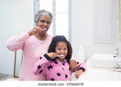 Portrait of grandmother and granddaughter brushing teeth in the bathroom at home