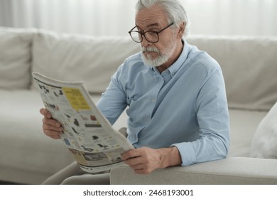 Portrait of grandpa with stylish glasses reading newspaper on sofa indoors - Powered by Shutterstock