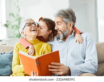 Portrait of grandparents and granddaughter having fun together reading a book at home - Powered by Shutterstock