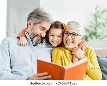 Portrait of grandparents and granddaughter having fun together reading a book at home - Powered by Shutterstock