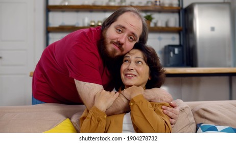 Portrait Of Grateful Adult Man Hug Smiling Middle-aged Mother Show Love And Care. Beautiful Senior Woman And Overweight Young Son Embracing Enjoy Weekend Family Time At Home Together
