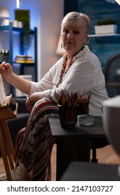 Portrait Of Gray Haired Older Hobby Artist Studying Shading Light On Still Life Using Model Vase In Home Studio. Retired Woman Drawing With Hb Pencil On Canvas In Front Of Easel While Sitting Down.