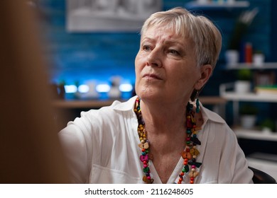 Portrait Of Gray Haired Senior Lady Wearing Colorful Necklace Drawing On Canvas In Home Art Studio. Elderly Woman Sketch Artist In Front Of Easel Working On Creative Freehand Charcoal Painting.