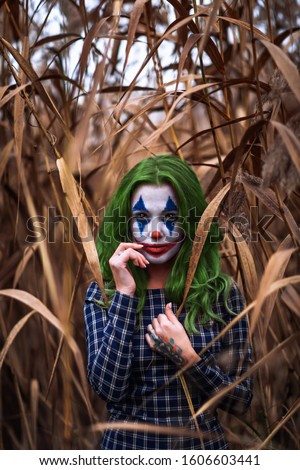 Portrait of a greenhaired girl with joker makeup on a orange leaves reeds background.