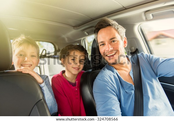 Portrait of a grey hair father with beard and his\
two kids in the car. The ten years old brother and sister are\
sitting in the back, they are wearing long sleeves shirts. The\
father have his seat\
belt