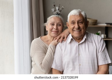 Portrait of grey-haired grandparents smile staring at camera feel satisfied, standing in living room, spend carefree retired life together. Happy marriage, pure love, good harmonic relations concept