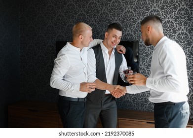 Portrait of groomsmen greeting groom with wedding day holding glasses and shaking hands standing in spacious room. Stag party with friends of fiance. - Powered by Shutterstock