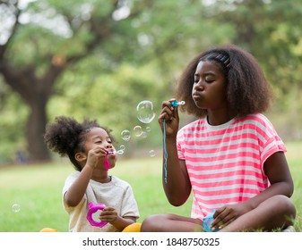 Portrait of group African American curly hairstyle girl playing blowing soap bubbles outdoor. Cute kid girl playing soap bubbles with green nature background in the park - Powered by Shutterstock