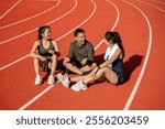 Portrait of a group of cheerful Asian athlete friends in sportswear, enjoying a conversation while resting on a sports track after training and running at a stadium on a sunny day.