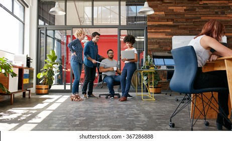 Portrait of group of creative people having a meeting with a laptop in a modern office. Business people having relaxed conversation over new project. - Powered by Shutterstock