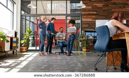 Portrait of group of creative people having a meeting with a laptop in a modern office. Business people having relaxed conversation over new project.