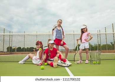 Portrait Of Group Of Girls As Tennis Players Holding Tennis Rackets Against Green Grass Of Outdoor Court. Stylish Young Teens Posing At Park. Sport Style. Teen And Kids Fashion Concept.