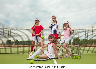 Portrait Of Group Of Girls As Tennis Players Holding Tennis Rackets Against Green Grass Of Outdoor Court. Stylish Young Teens Posing At Park. Sport Style. Teen And Kids Fashion Concept.