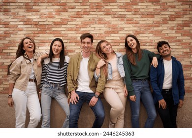 Portrait group of international cheerful friends posing together hugging looking smiling at camera. Happy generation z people leaning on brick wall outdoor. Relationships, friendship and community