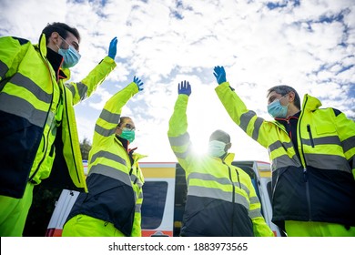 Portrait of a group of paramedics at the end of their shift in front of the ambulance while they high-fives in the air dressed in uniform and wearing a mask for protection from Coronavirus, Covid-19 - Powered by Shutterstock