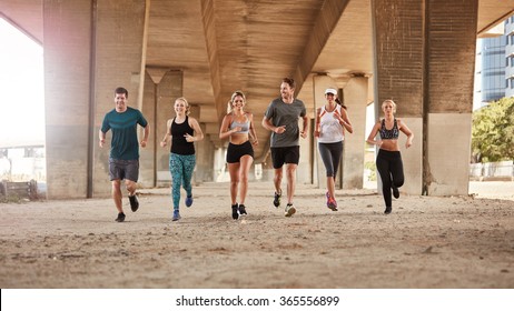 Portrait Of Group Of Runners From Running Club Under A Bridge. Young Men And Women Jogging Together.