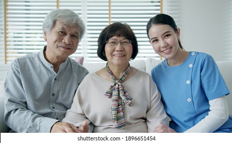 Portrait group shot of happy senior asian couple with in home nursing care sitting smile at sofa couch looking at camera with enjoy retirement or quarantine time. Asia adult older people lifestyle.