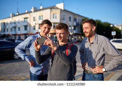 Portrait of a group of smiling friends, preparing for making selfie on camera on urban background.
