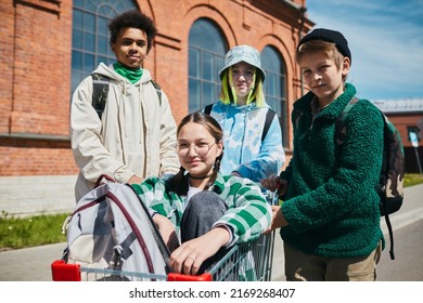 Portrait Of Group Of Teen Boys And Girls Looking At Camera While Riding On Shopping Cart On The Street