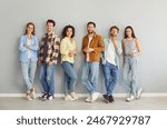 Portrait of a group of young happy smiling friends students or colleagues in casual clothes standing together posing isolated on a gray background and looking confidently and positively at camera.