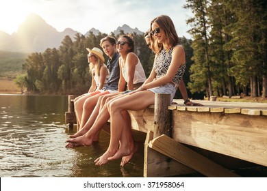 Portrait of group of young people sitting on the edge of a pier, outdoors in nature. Friends enjoying a day at the lake. - Powered by Shutterstock