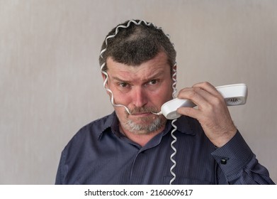 Portrait of a grown man wrapping a telephone cord around his head. A man in a blue striped shirt with a puzzled face. The man bites down on the white wire.  Indoors. - Powered by Shutterstock