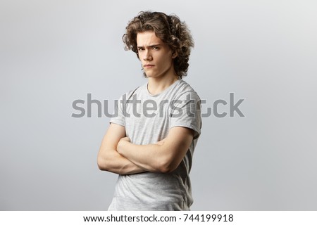 Portrait of grumpy angry young man posing in studio with arms folded, feeling insulted while having quarrel with his girlfriend. Reluctant guy expressing his unwillingness towards doing something