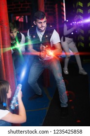 Portrait of guy in colored beams of laser guns during laser tag game on dark arena