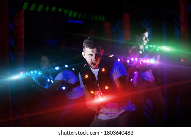 Portrait of guy in colored beams of laser guns during laser tag game on dark arena