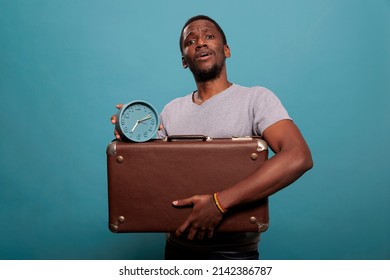 Portrait Of Guy Holding Retro Suitcase And Clock In Front Of Camera, Preparing To Leave On Journey Trip. Casual Man With Briefcase Luggage Checking Time On Watch, Running Late On Vacation.