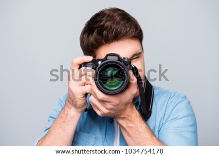 Portrait of guy in jeans shirt looking at photo camera, shooting photographs during excursion, making photosession over gray background